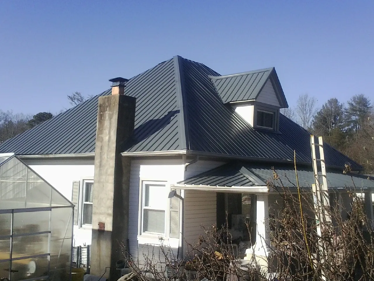 Dark blue standing seam metal roof on a white farmhouse with dormer — Slate & Tile Roof Repair by Roofing Brothers in Hawk Springs