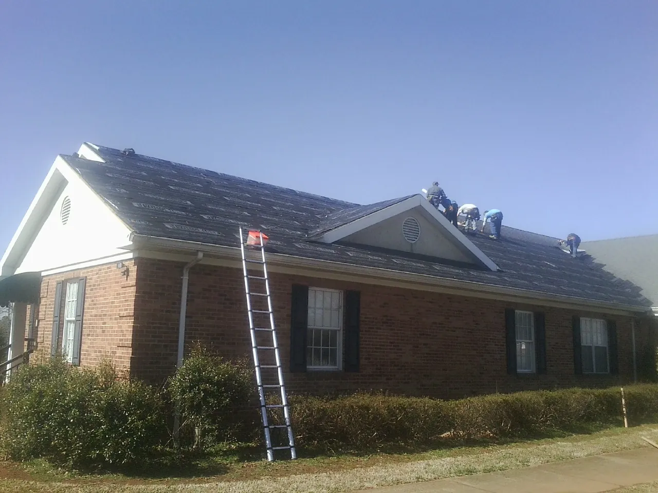 Crew tearing shingles off a brick ranch roof with a ladder set — Metal Roof Repair work by our crew in Hawk Springs