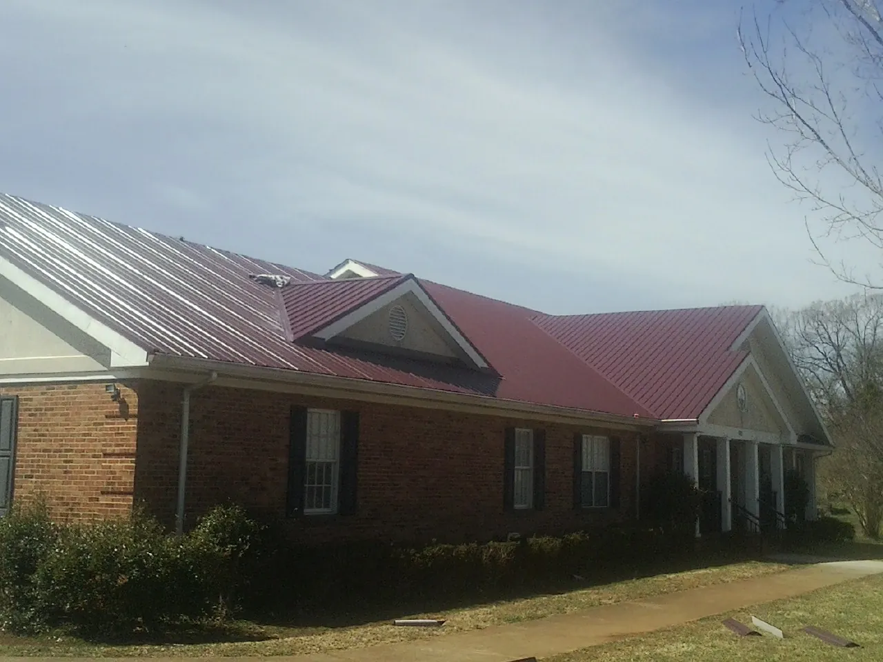 Red metal roof with gabled entries on a long brick building, from a Hail Damage Roof Repair job in Hawk Springs