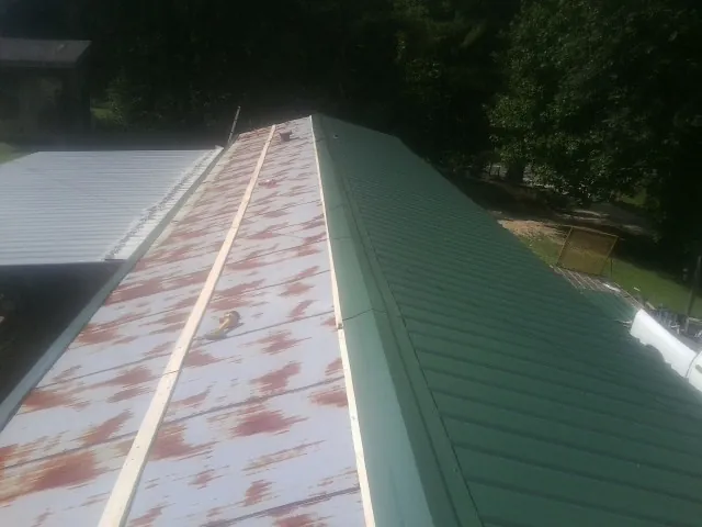 Old rusted panels beside newly installed green metal roofing — Wind Damage Roof Repair by Roofing Brothers in Hawk Springs