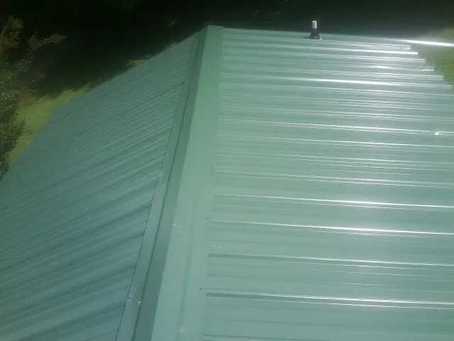 New green metal panels meeting at the ridge of a roof — Flat Roof Repair work by our crew in Hawk Springs