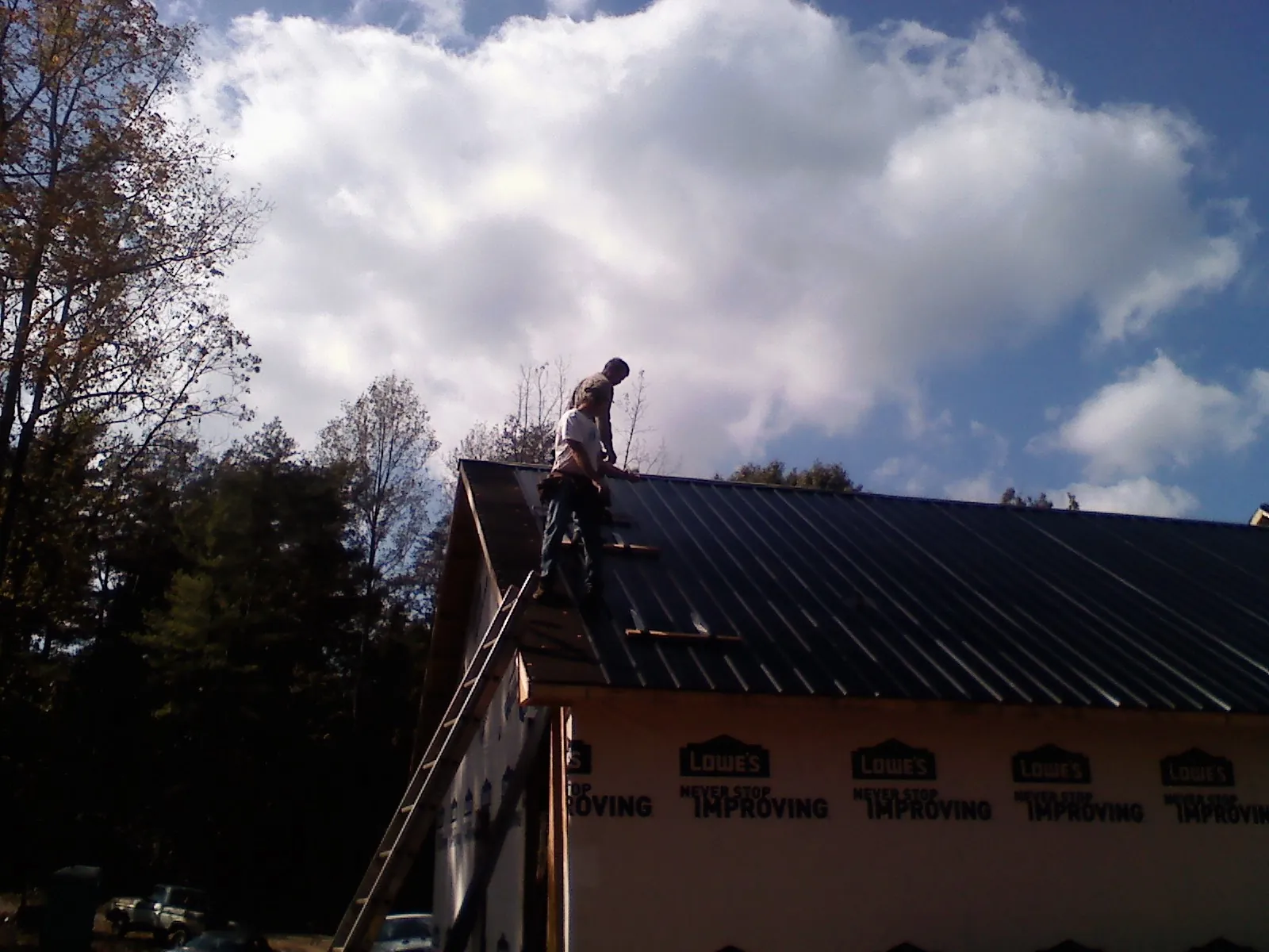 Roofer fastening dark metal panels high against a cloudy sky, from a Roof Inspection job in Hawk Springs