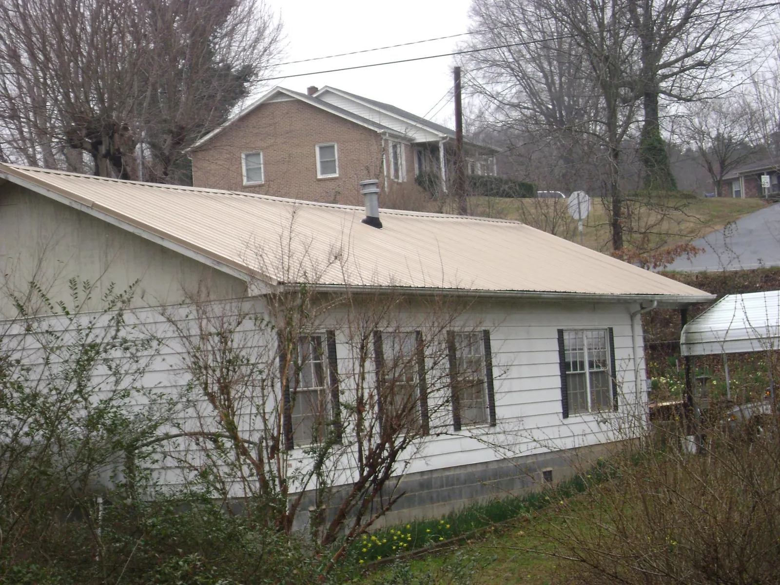 Tan metal roof on a white sided house set into a hillside — Commercial Roofing by Roofing Brothers in Hawk Springs